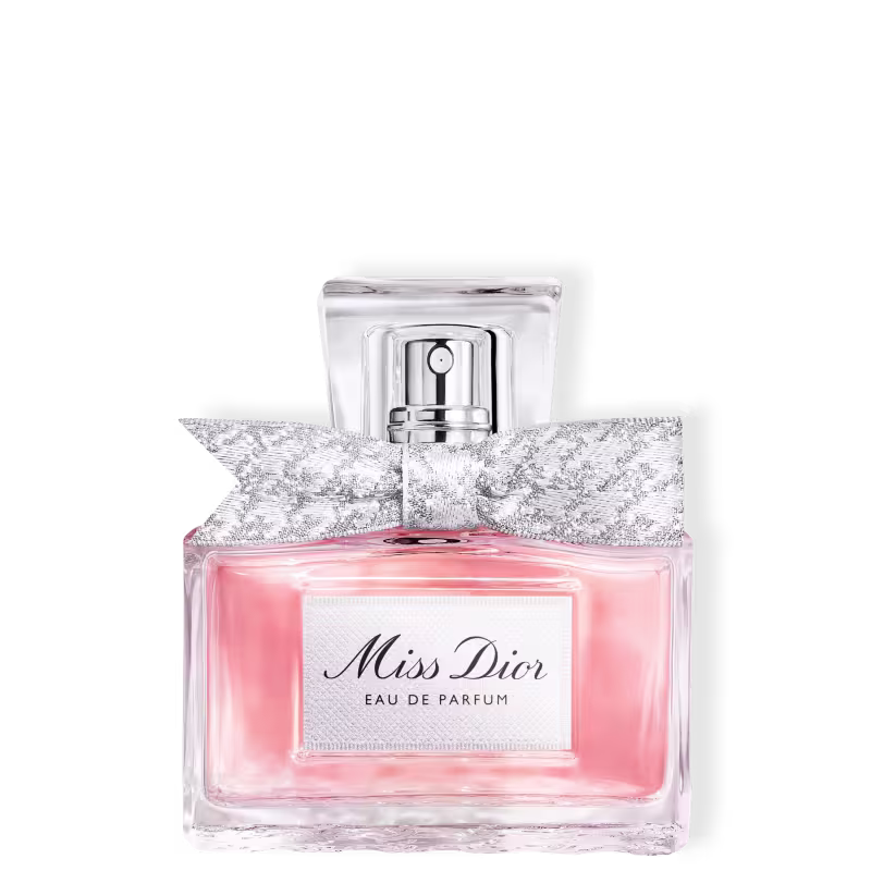Frasco de perfume Miss Dior em formato retangular com tampa prateada. Embalagem com detalhes em renda branca e rosa claro, com texto "Miss Dior Eau de Parfum" em destaque.