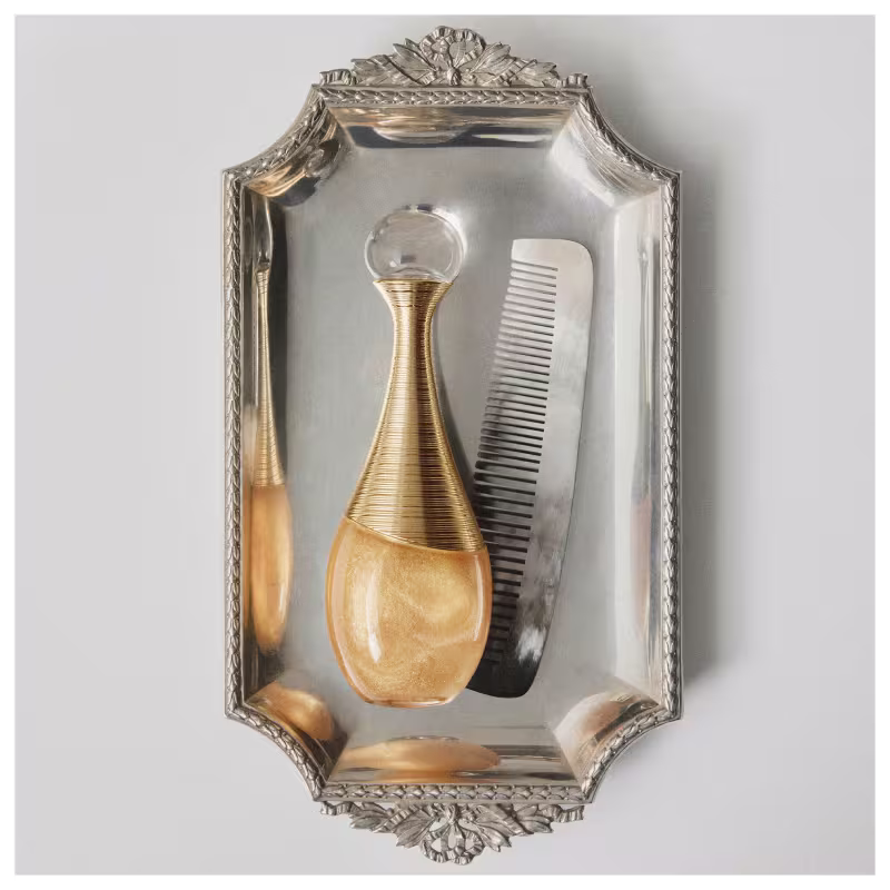 Frasco de perfume para cabelo Dior em formato de gota, com corpo dourado e detalhes em fios dourados entrelaçados, tampa transparente redonda. Embalagem elegante e sofisticada.