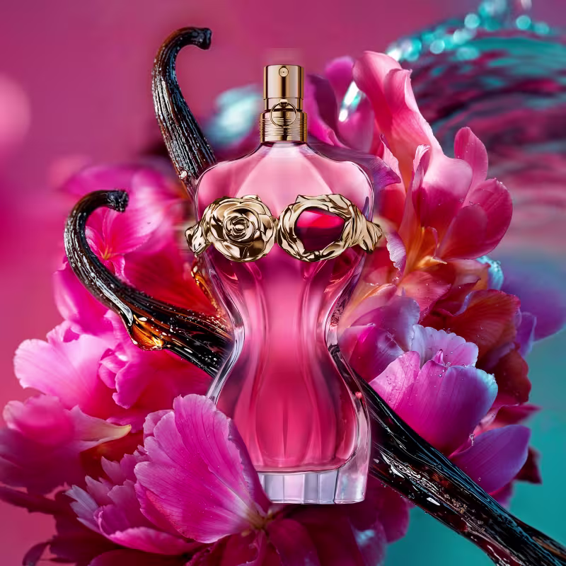 O ambiente retratado é uma composição floral vibrante, com pétalas rosas e azuis, que enquadram um frasco de perfume da marca Jean Paul Gaultier.