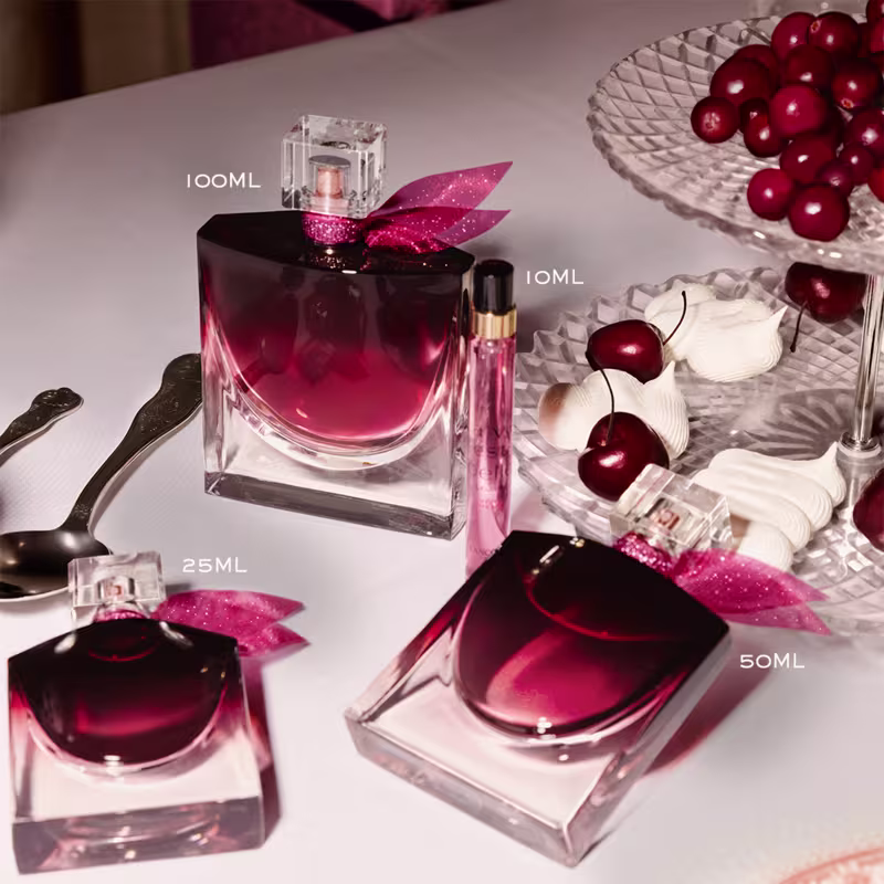 Ambiente elegante e sofisticado com produtos de perfumaria da marca Lancôme em tons de rosa e vermelho, complementados por detalhes decorativos como cerejas e taças de cristal, sugerindo uma ocasião especial.