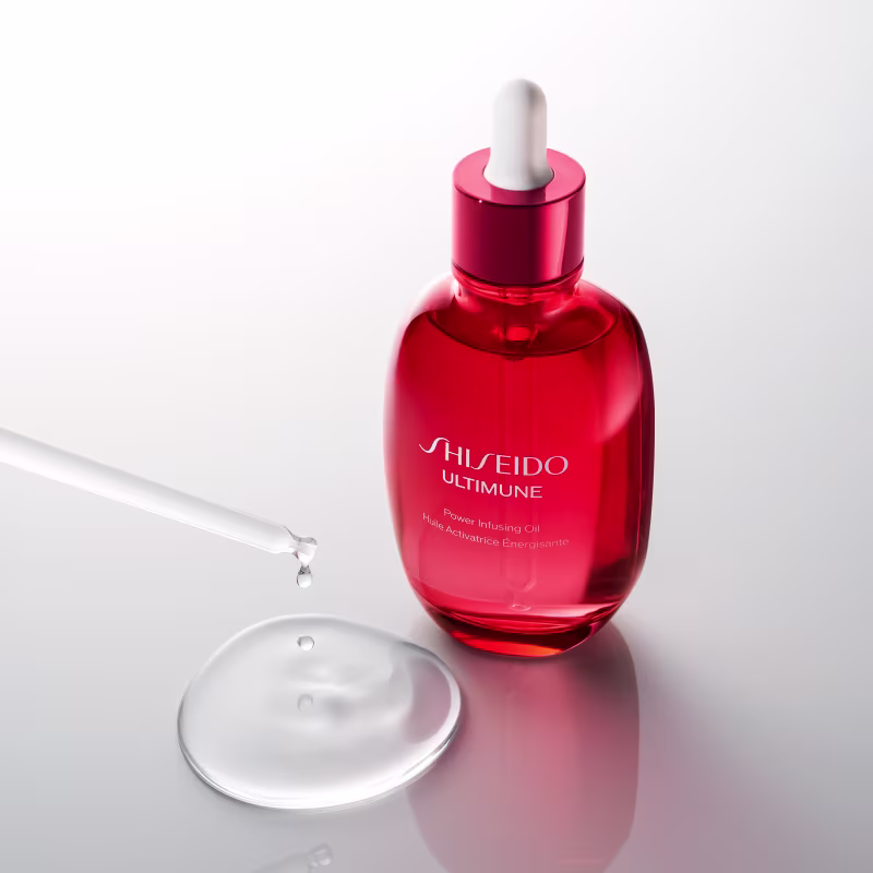 Frasco de vidro vermelho com conta-gotas da marca Shiseido, sobre superfície branca refletiva, com gota d'água suspensa acima.