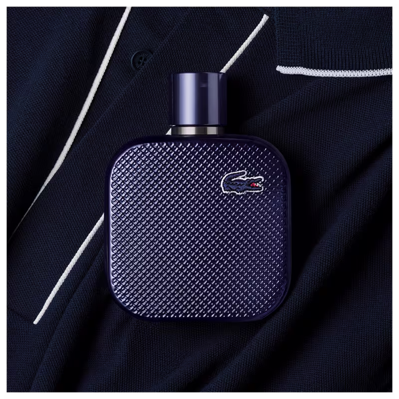 Frasco de perfume Lacoste de cor azul escuro, com textura de couro e logotipo da marca em destaque. Embalagem elegante e minimalista, com tampa preta.