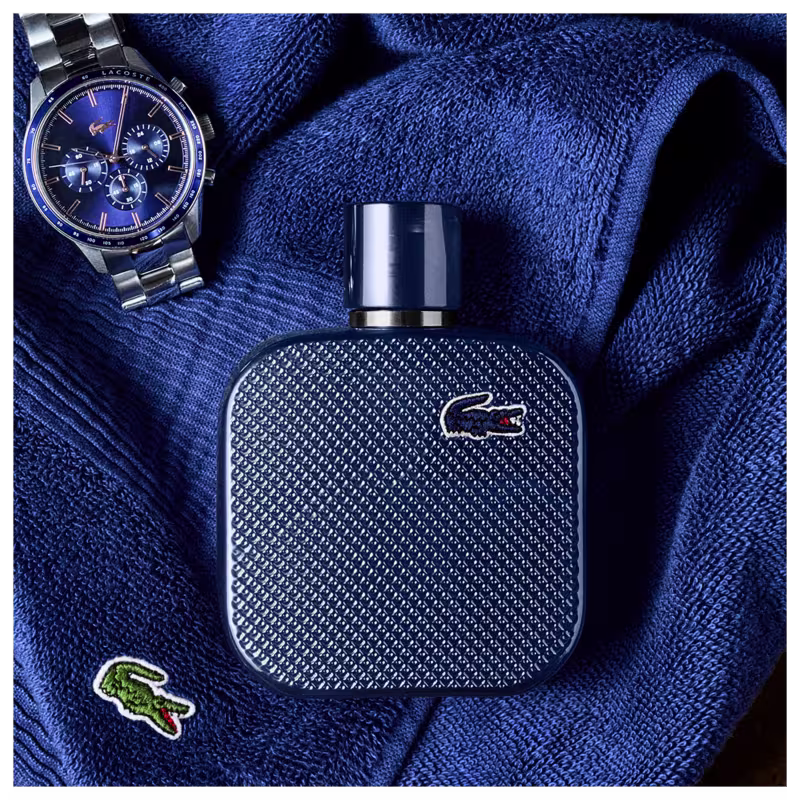 Frasco de perfume Lacoste de cor azul escuro, com textura de couro e logotipo da marca em destaque. Embalagem elegante e minimalista, com tampa preta.