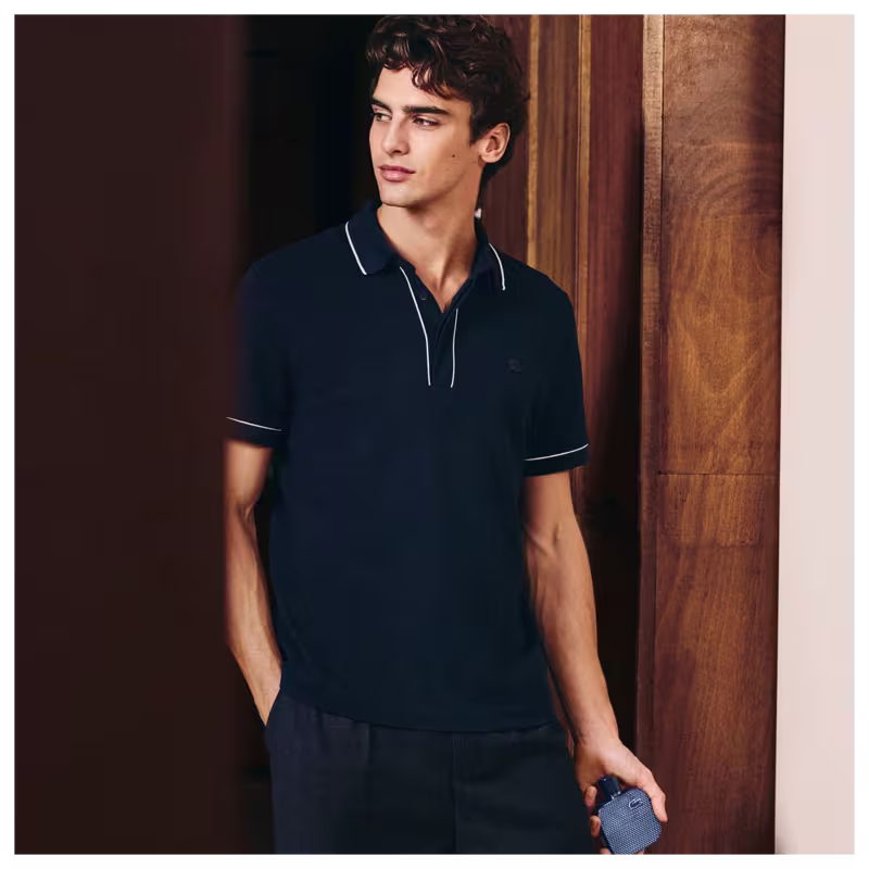 Frasco de perfume Lacoste de cor azul escuro, com textura de grade e logotipo da marca em destaque. Embalagem cilíndrica com tampa preta, apresentando design elegante e sofisticado.