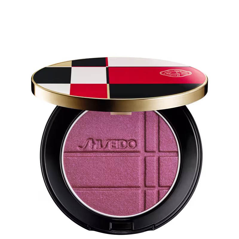 Pó compacto de maquiagem da marca Shiseido, em embalagem redonda com tampa dourada, com design xadrez em vermelho, branco e preto.