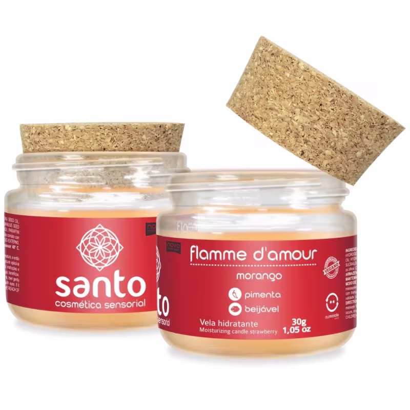 O produto apresentado são velas hidratantes da marca Santo Cosméticos. Há dois pequenos frascos de vidro transparente contendo uma vela com rótulo vermelho dentro. As tampas são de cortiça natural. Os rótulos indicam que o aroma é de morango.