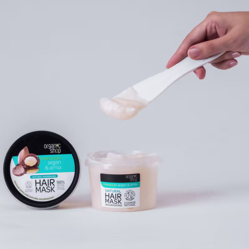 A imagem mostra a máscara capilar e uma mão segura uma espátula branca.