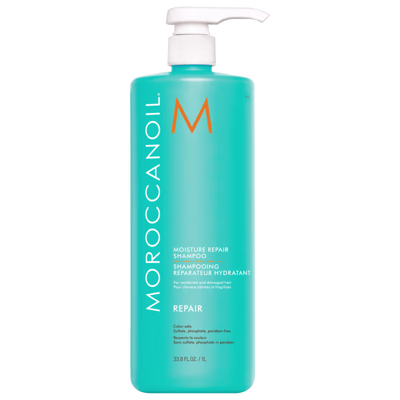 A imagem mostra o Shampoo Moroccanoil Repair Moisture 1L, um frasco de plástico azul turquesa e com uma bomba dosadora branca na parte superior. O logo traz um M em tom de laranja e o nome da marca em branco.