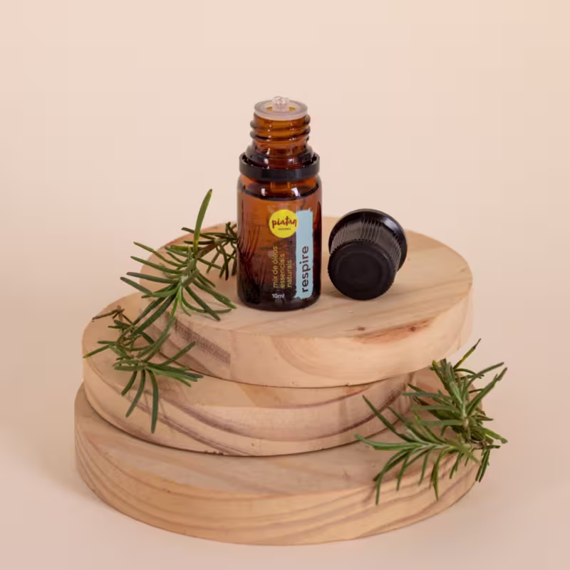 A imagem mostra o frasco do óleo essencial respire sobre bases de madeira. Ao redor há galhos de alecrim.