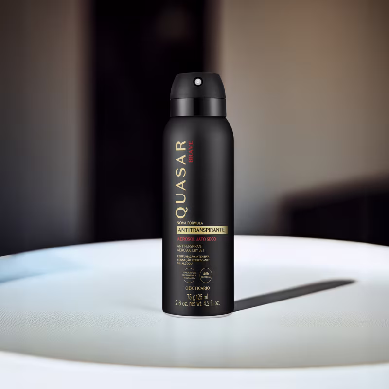 A embalagem é preta, com o nome da marca "Quasar" e a indicação "Nova Fórmula Antitranspirante" impressos em letras douradas. O frasco possui um formato cilíndrico e um bico pulverizador na parte superior.