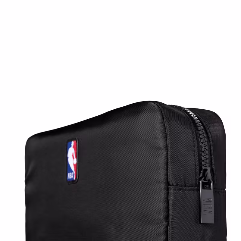 Esta imagem mostra um nécessarie preto com o logotipo da NBA (National Basketball Association) e O Boticário MEN  impresso nela. Tem um design simples e minimalista, com um zíper principal.
