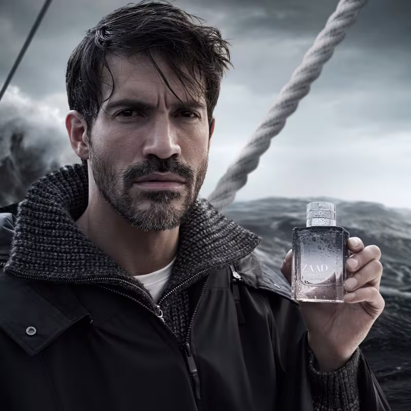 Ambiente marítimo tempestuoso com homem segurando frasco Zaad, sugerindo sua utilização em condições climáticas adversas. Predominância de tons escuros e sombrios.