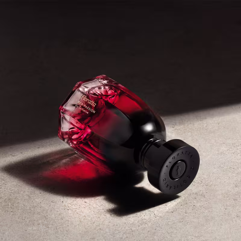 O produto apresentado é um frasco da linha Floratta Red Passion, com um design geométrico e uma coloração vermelha intensa. O frasco possui um formato angular e uma tampa preta com o logotipo da marca.