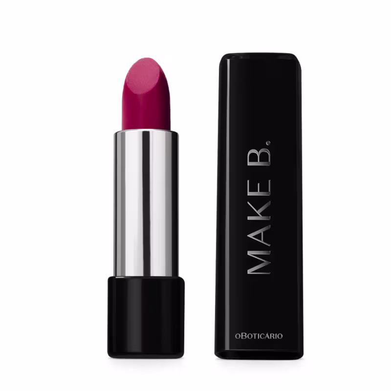O produto é um batom de cor rosa intenso em uma embalagem cilíndrica prateada. Ao lado está a caixa preta do batom com o logotipo "MAKE B." em letras maiúsculas. O nome "oBoticario" também está impresso na caixa.