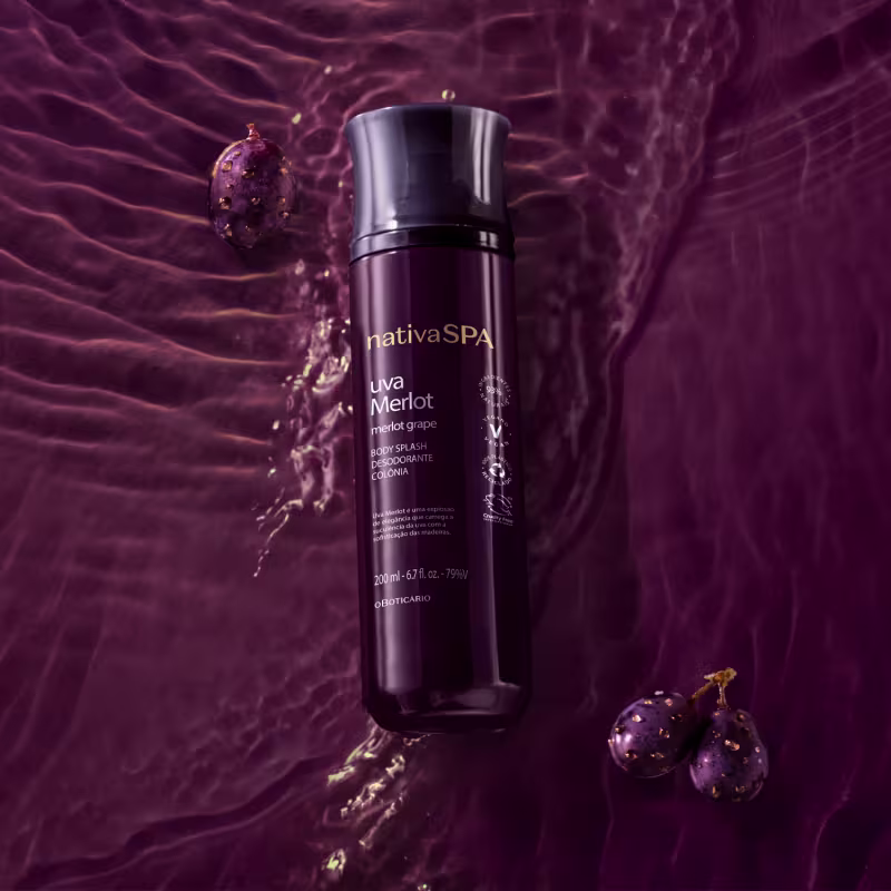 O frasco é preto, com um design elegante e moderno. Ao lado do frasco, há alguns frutos de uva roxa, que parecem ser a inspiração para o aroma deste produto. A imagem tem um fundo roxo escuro, criando um ambiente sofisticado e luxuoso.