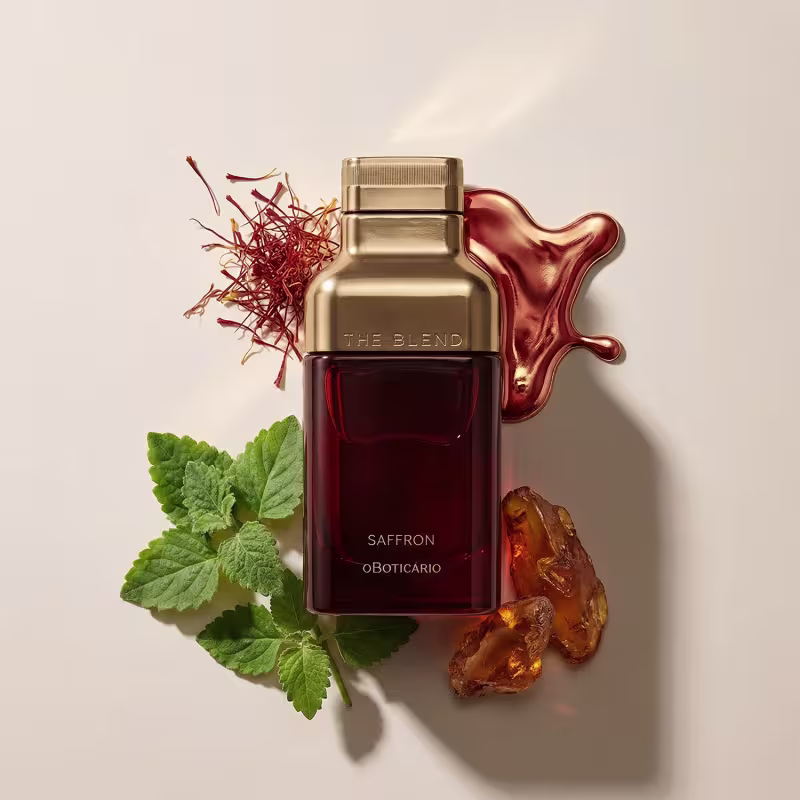 Ambiente de luxo e sofisticação com o frasco dourado da marca The Blend, contendo a fragrância Saffron, rodeado por ingredientes naturais como açafrão, folhas verdes e âmbar, em um cenário elegante e minimalista.