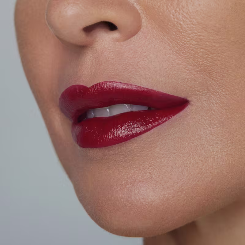 Lábios pintados com batom vermelho brilhante em primeiro plano, sobre fundo claro e liso.