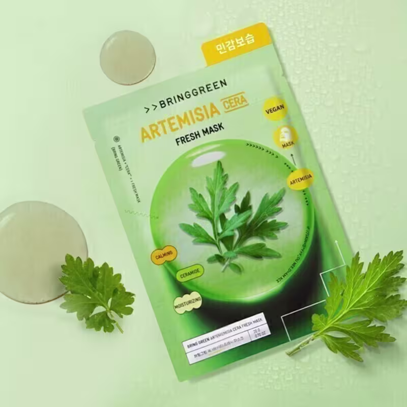 Máscara facial da marca Bringgreen, com embalagem verde e amarela, apresentando folhas verdes de artemísia como ingrediente principal. O produto é descrito como "Fresh Mask" e possui rótulos em coreano e inglês.