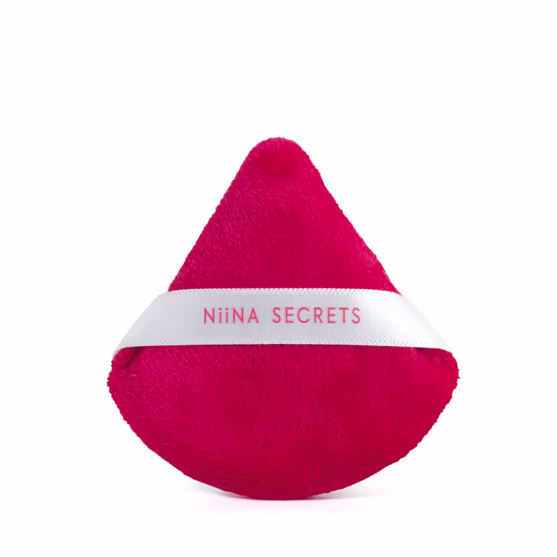 Esponja de maquiagem triangular de gota de cor vermelha intensa em material aveludado. Possui uma faixa branca com o texto Niina Secrets. O produto tem aparência macia e compacta.