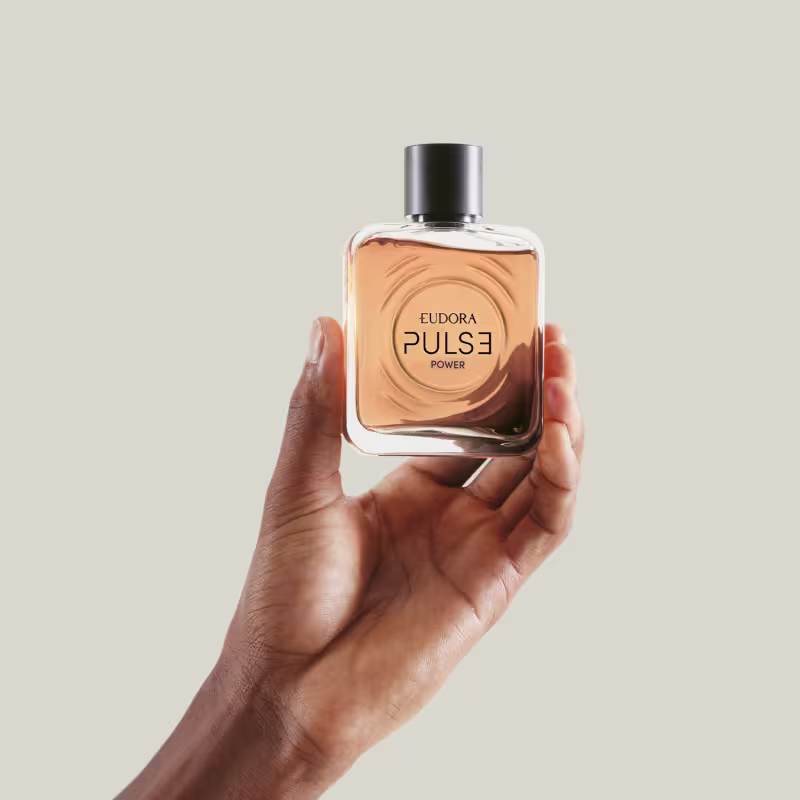 O produto apresentado na imagem é um frasco do Desodorante Colônia Pulse Power. O frasco possui um formato cilíndrico com uma tampa preta. O produto é segurado por uma mão masculina.