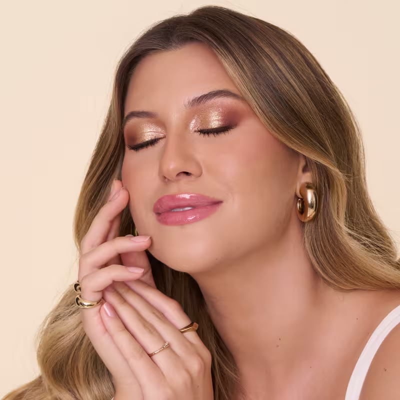 Ambiente de beleza com iluminação suave e tons neutros, destacando o rosto da Niina com maquiagem delicada e joias douradas, sugerindo um produto de cuidados com a pele da marca Niina Secrets.