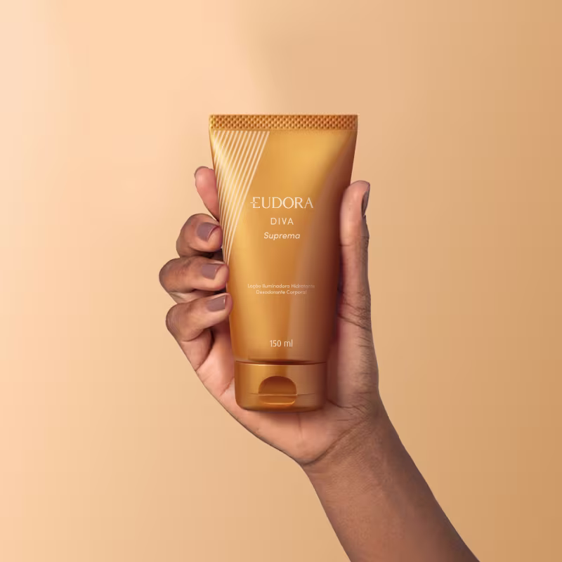 O produto apresentado é um desodorante corporal da linha Diva Suprema. O recipiente é um tubo dourado com detalhes em relevo e o nome da linha "Diva Suprema" impresso. O tubo possui 150 ml de volume e é descrito como um loção iluminadora hidratante.