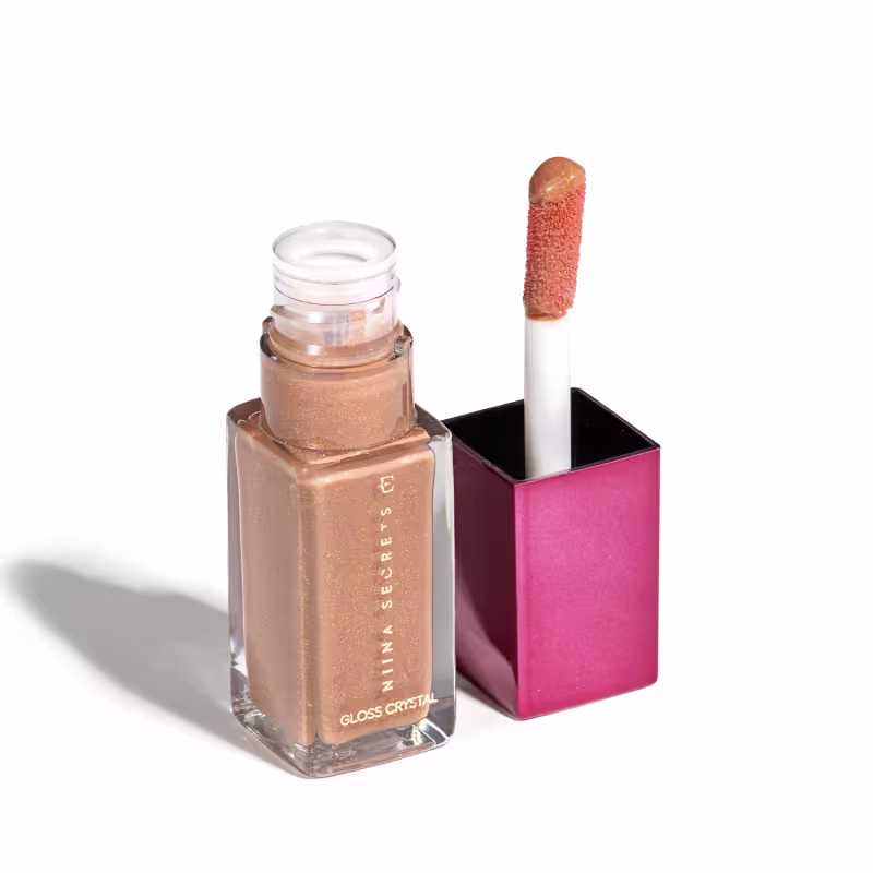 Frasco de cristal com gloss labial dourado da marca Niina Secrets, embalado em frasco de vidro, quadrado, transparente com tampa rosa. O produto apresenta um aplicador de espuma na ponta.