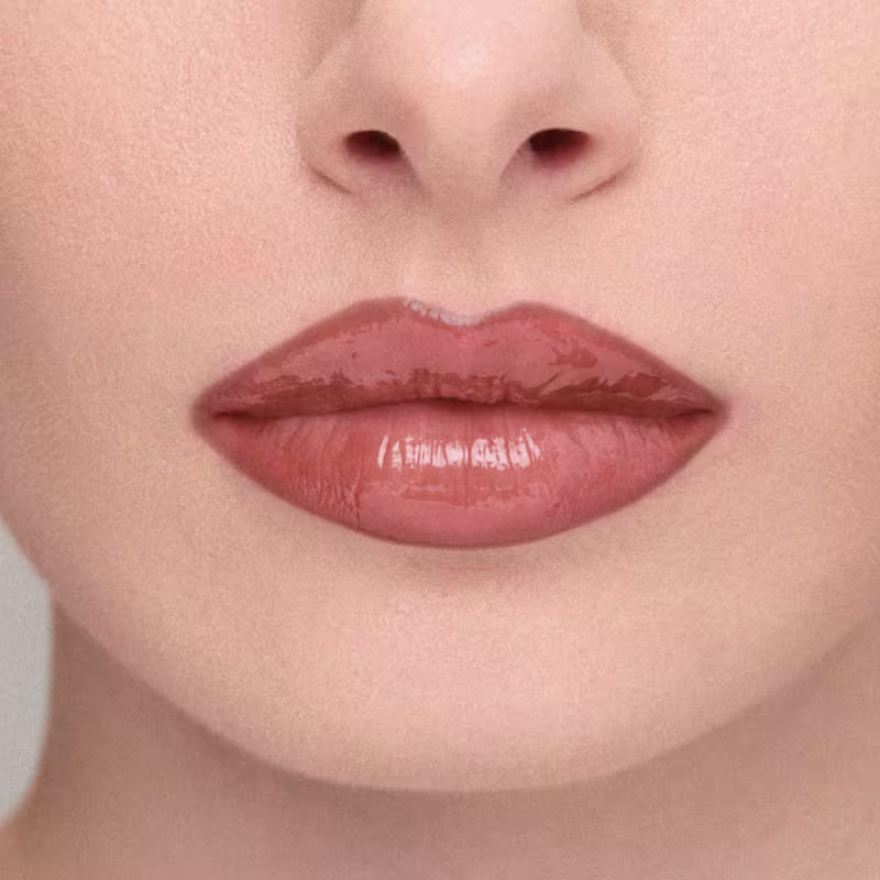 Imagem em close-up de lábios de uma modelo, mostrando o efeito do Gloss Labial: Lábios amarronzado com brilho, em primeiro plano, sobre fundo neutro.
