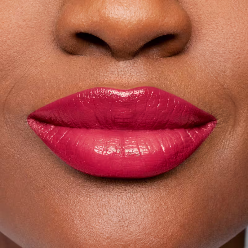 Imagem com foco nos lábios femininos com batom vermelho, com um acabamento lustroso e brilhante. O foco está nos lábios, que ocupam a maior parte da imagem.
