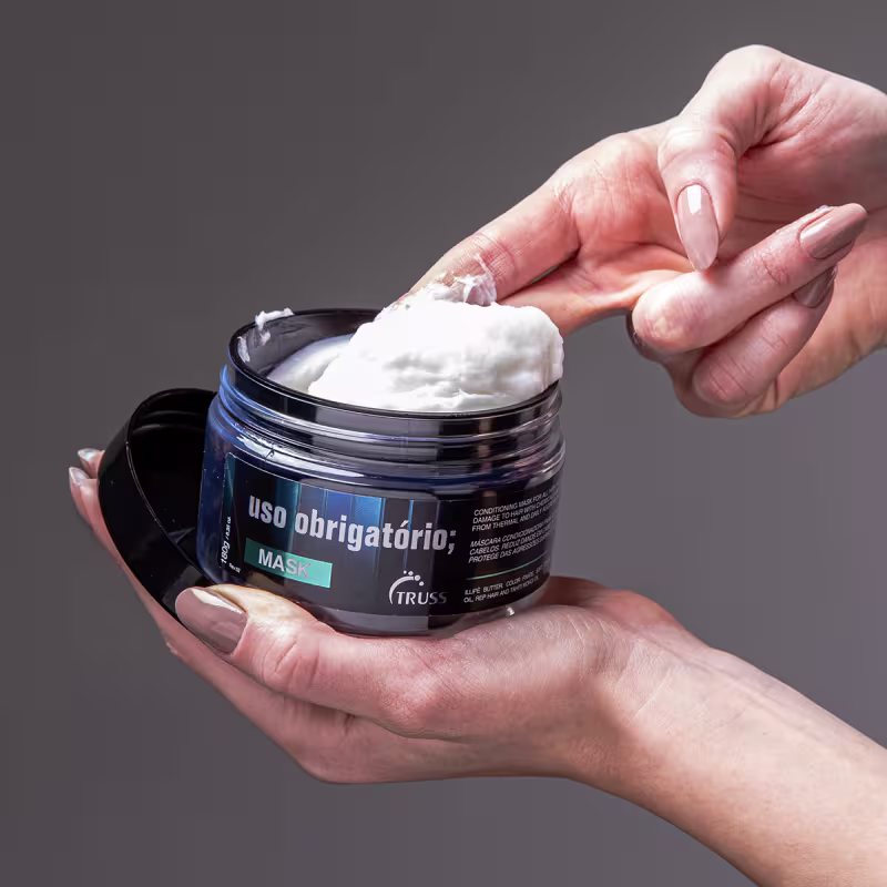 A imagem mostra uma máscara capilar, da marca Truss, linha Uso Obrigatório. O produto está aberto, sendo possível observar o seu conteúdo, de aspecto branco, com textura densa e cremosa.