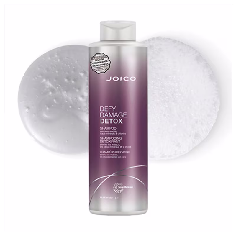 A imagem mostra o Shampoo Joico Defy Damage Detox e no fundo uma amostra com a textura e cor do produto, em tonalidade branca e espuma cremosa.
