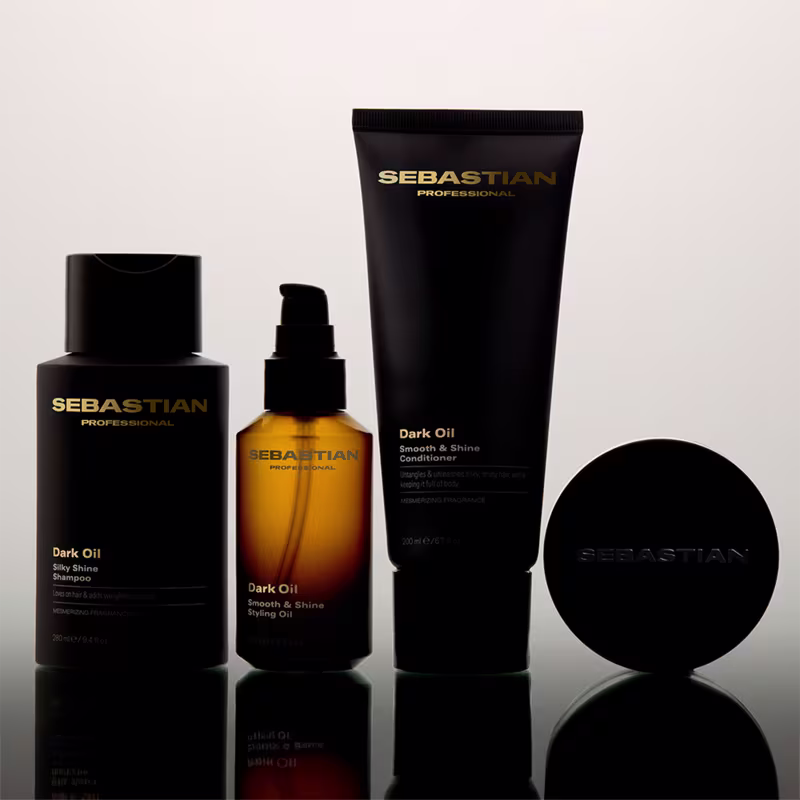 Produtos da marca Sebastian Professional, incluindo um frasco de shampoo, um frasco de óleo para cabelos, um tubo de condicionador e uma embalagem preta redonda, todos em cores preto e dourado.