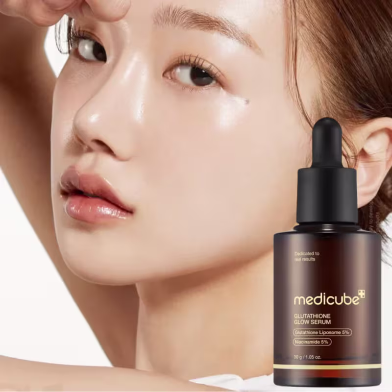A imagem mostra uma mulher aplicando um sérum facial da marca Medicube, com destaque para a embalagem preta do produto. O ambiente sugere um contexto de cuidados de beleza e tratamento da pele.