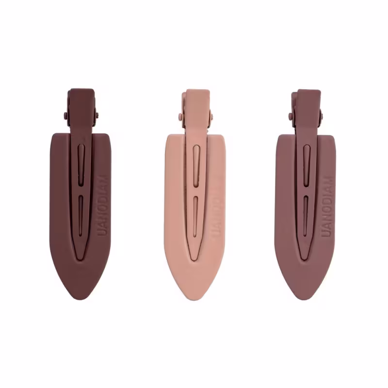 A imagem mostras três presilhas de cabelo plásticas em diferentes tons de nude. Cada pinça tem um formato alongado e pontiagudo, com uma abertura na parte superior para prender os cabelos.