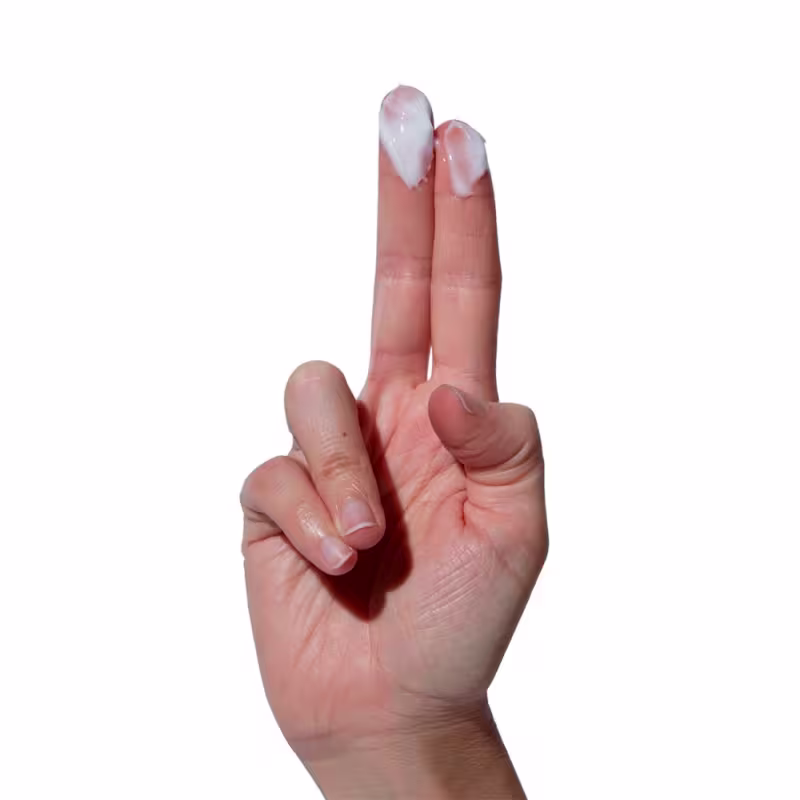 A imagem mostra uma mão com dois dedos apontados para cima, neles há uma quantidade pequena do creme hidratante.