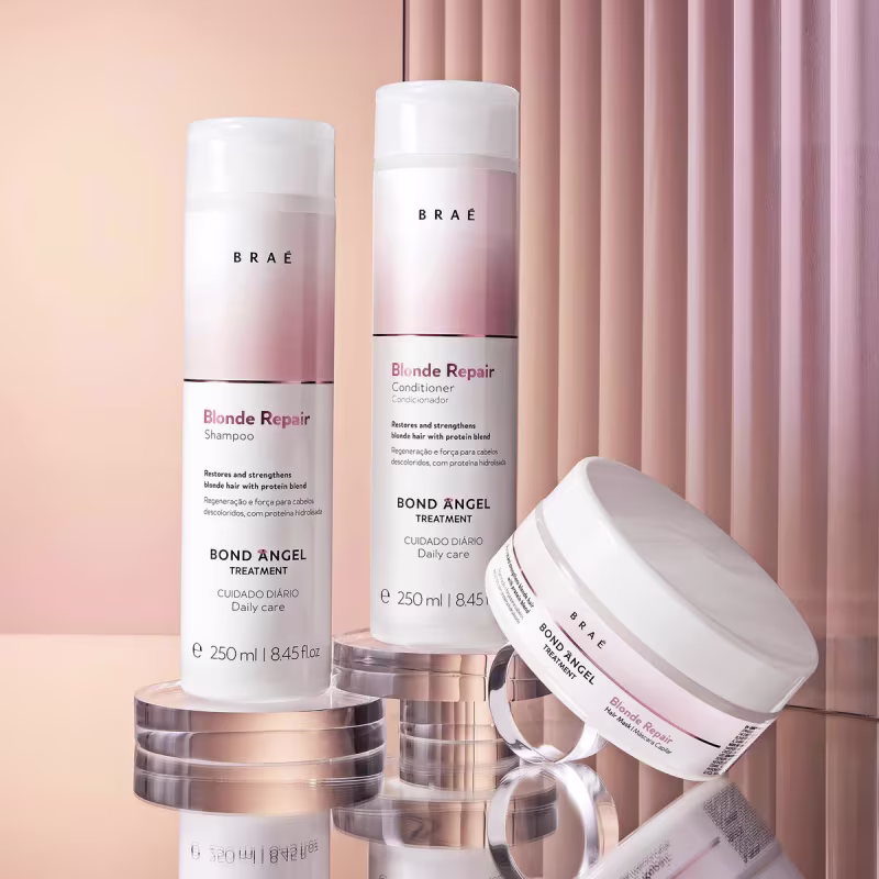 Produtos para cuidados capilares da marca Brae. Shampoo e condicionador da linha Blonde Repair em frascos cilíndricos de plástico branco e rosa. Também há um tratamento capilar Bond Angel em embalagem cilíndrica branca.