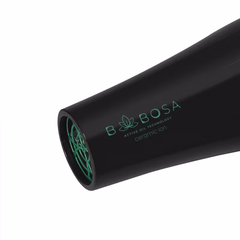 A imagem mostra no detalhe o cilindro de ar do secador de cabelo. Ele possui a cor preta com detalhes vazados em verde. Na lateral traz escrito a linha, com um design sofisticado e minimalista.