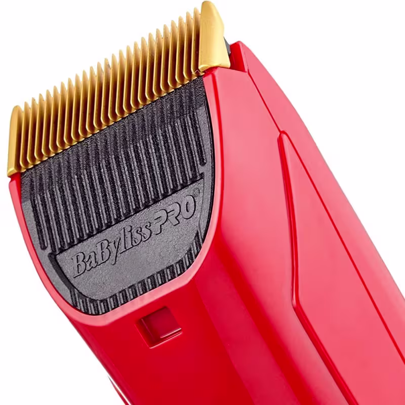 Máquina de corte da marca BaByliss PRO. O corpo é vermelho brilhante com detalhes dourados. A lâmina de corte tem uma formação ondulada dourada. O design é compacto e ergonômico, adequado para uso profissional em salões de beleza.