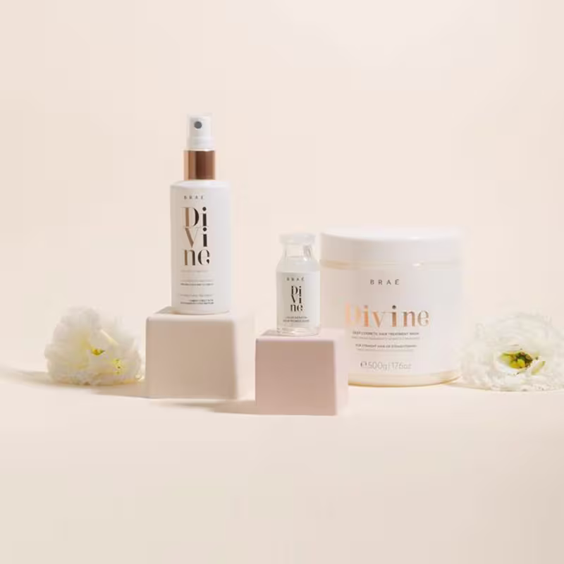 A imagem mostra produtos de cuidados capilares da marca Braé. Há um frasco spray grande de cor branca com detalhes em cobre, um frasco menor do mesmo estilo e uma lata ou pote grande com a palavra "Divine" impressa.