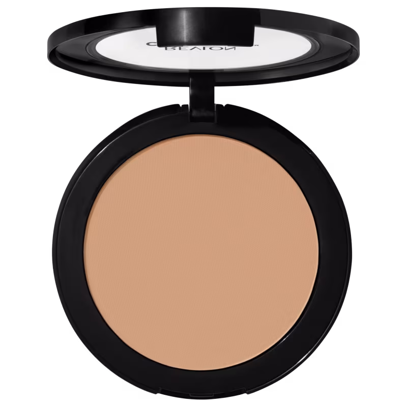 Pó compacto de maquiagem Revlon em embalagem redonda preta. A superfície do pó tem uma cor bege claro uniforme. A tampa transparente exibe o logotipo "Revlon" em letras brancas. O produto apresenta um design minimalista e elegante.