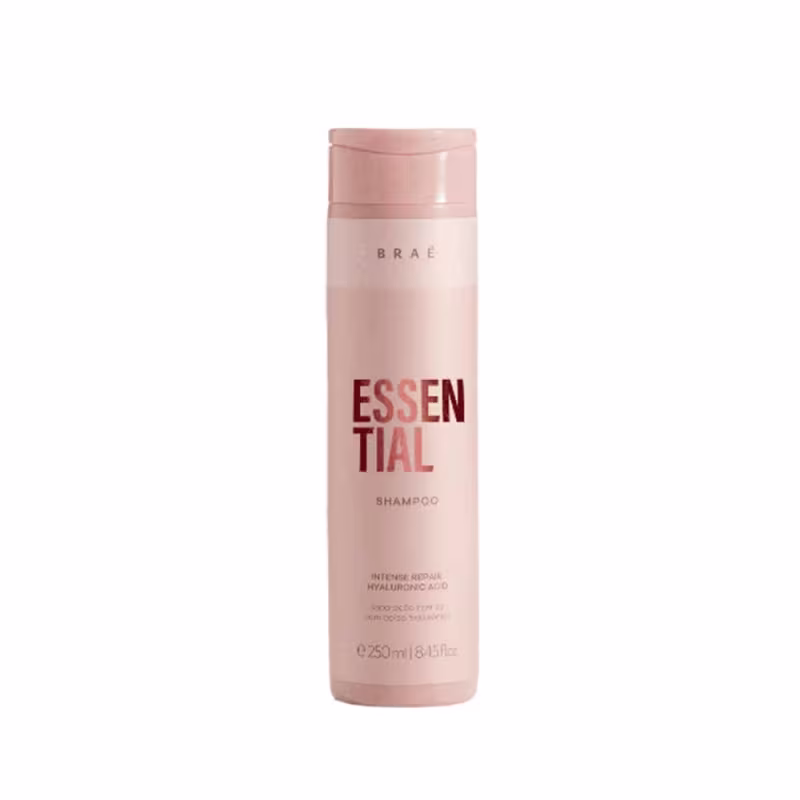 Shampoo Essential da marca Braé. Embalagem cilíndrica de plástico transparente na cor rosa claro. Rótulo com o nome do produto "Essential" em letras vermelhas grandes e o nome da marca "Braé" em letras menores acima.
