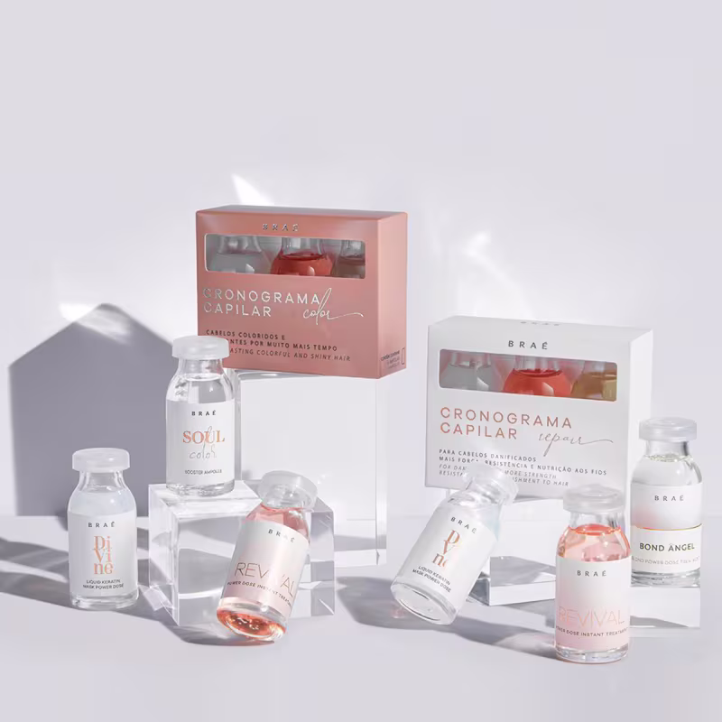 A imagem mostra uma variedade de produtos de cuidados capilares da marca Brae. Há frascos de vidro transparente contendo líquidos de diferentes tons de rosa e laranja. Os produtos são ampolas do kit de cronograma capilar.