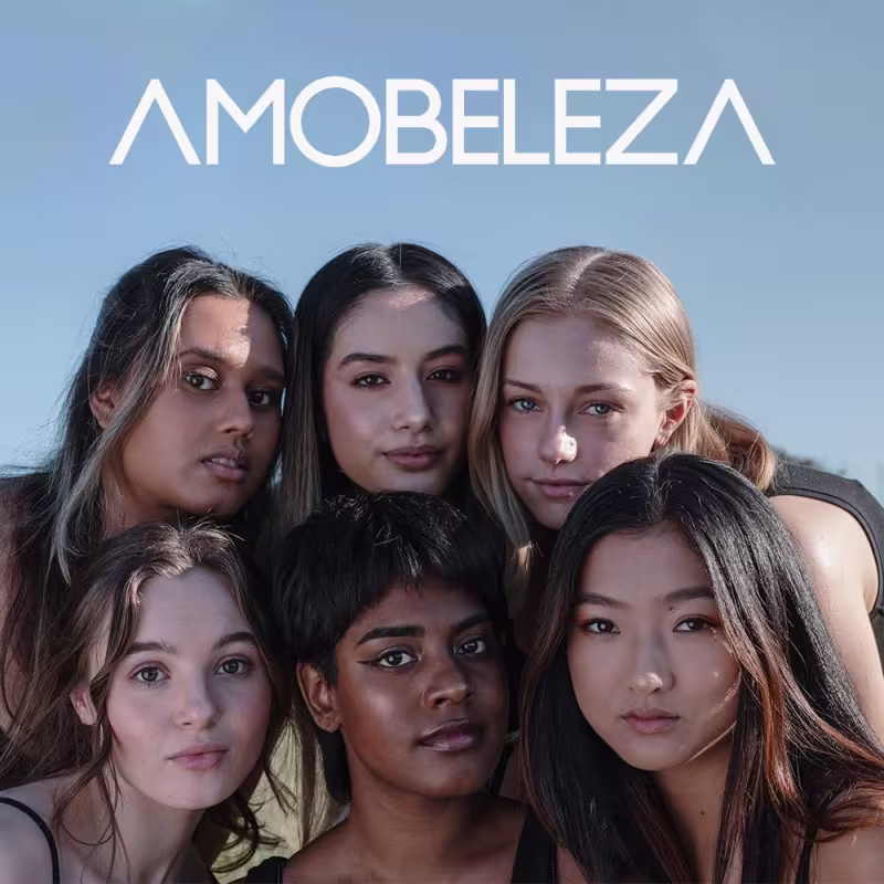 A imagem mostra um grupo de cinco modelos mulheres de diferentes etnias e tons de pele, posando juntas. Elas têm expressões sérias e maquiagem natural. No topo da imagem, está escrito "AMOBELEZA" em letras maiúsculas brancas contra um fundo azul claro.