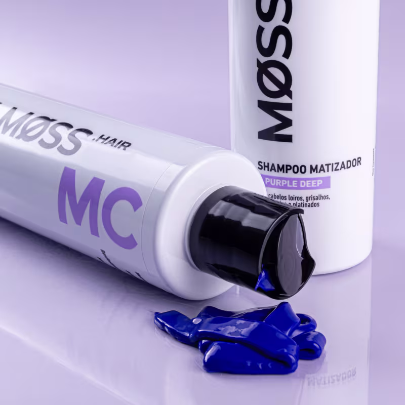 A imagem mostra dois produtos da linha Purple Deep de Moss. Um é um shampoo matizador e o outro é uma Máscara Capilar, este último apresenta uma porção da máscara à sua frente com um tom do pigmento roxo azulado intenso do matizador.