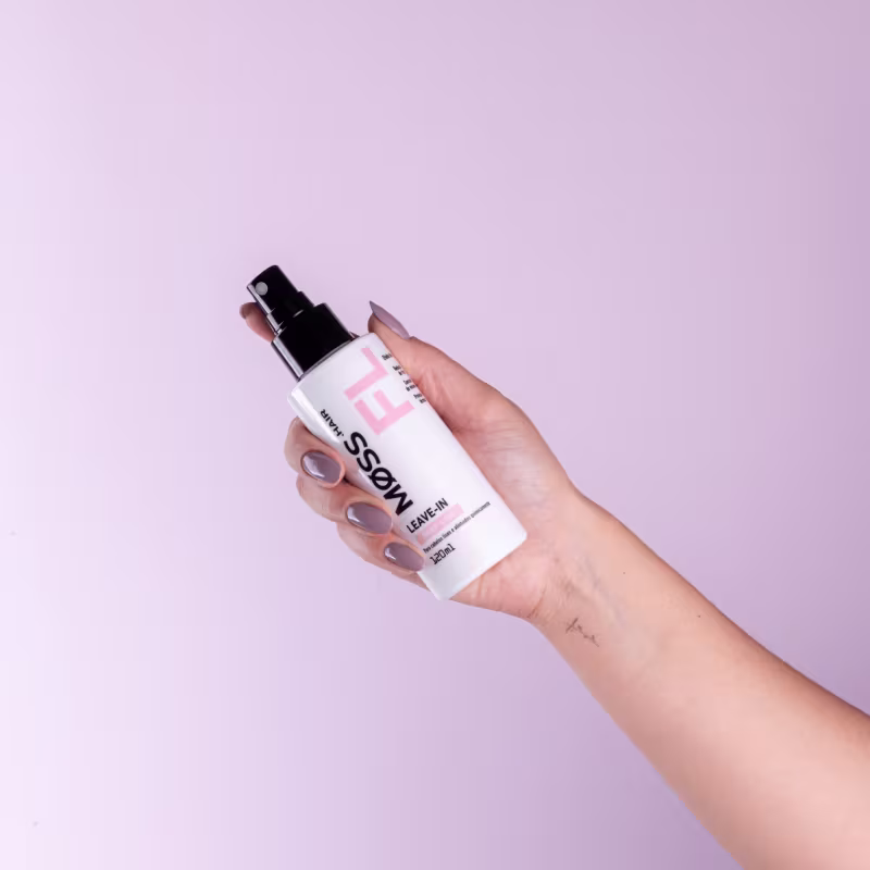 A imagem mostra uma mão segurando o frasco do leave-in deep liss em um fundo lilás.
