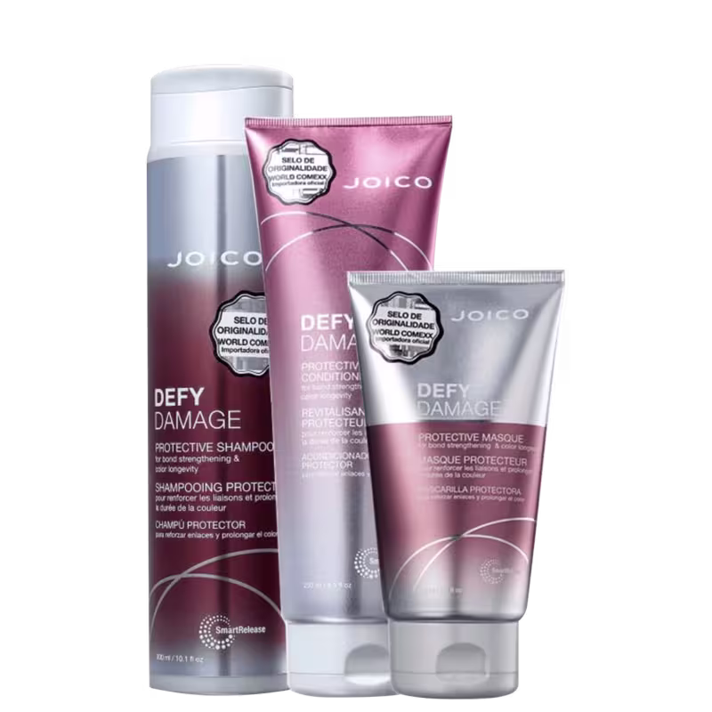 A imagem mostra três produtos da linha "Defy Damage" da marca Joico: shampoo, condicionador e máscara capilar. As embalagens são roxas com tons prateados e letras brancas.