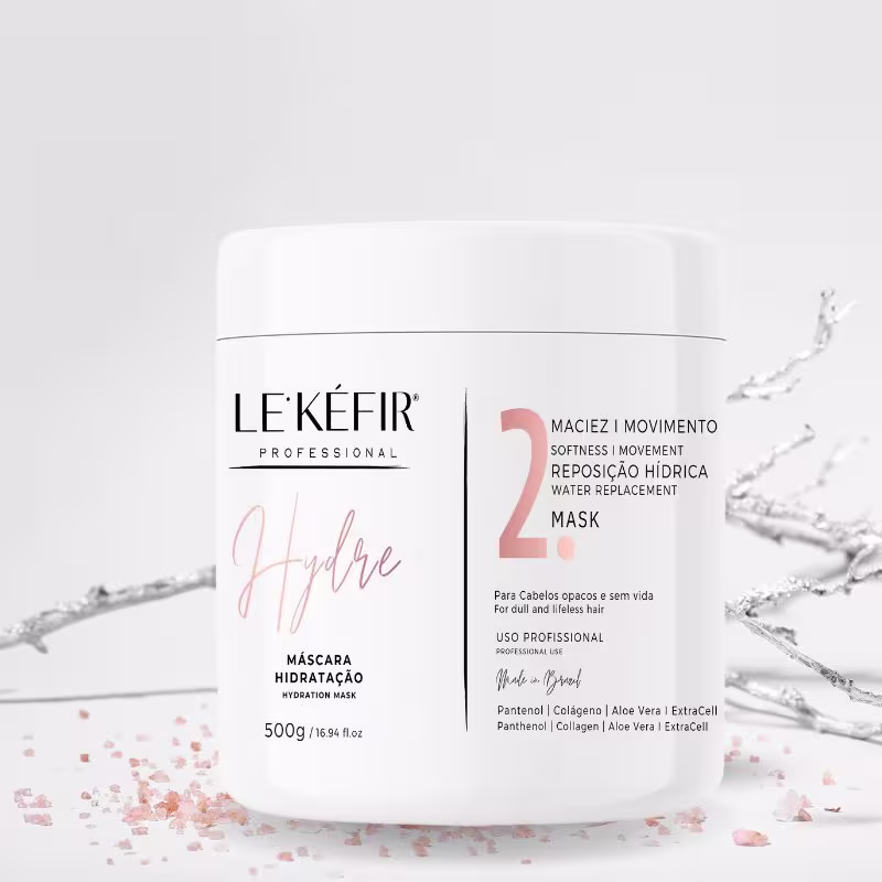 A imagem mostra a máscara de hidratação "Hydre" em um pote branco em um fundo branco com pequenos detalhes cor de rosa espalhados, criando um visual elegante e clean.