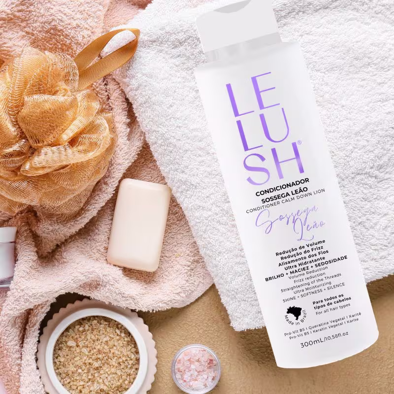 A composição da imagem transmite uma atmosfera aconchegante e relaxante, remetendo aos momentos de cuidados pessoais e autocuidado. Nela há a embalagem do condicionador sobre uma toalha branca ao lado de itens de higiene pessoal, como sabonetes e sais.