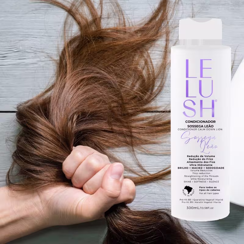 A imagem mostra uma mão segurando delicadamente alguns fios de cabelo longos e ondulados de cor castanha. Ao lado, há um frasco branco do condicionador para cabelos da linha Lelush Sossega Leão.