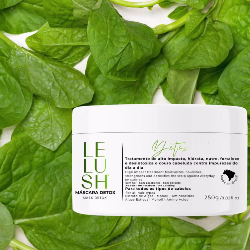 A imagem mostra a embalagem da máscara capilar posicionada sobre folhas verdes brilhantes de uma planta, criando um ambiente natural e refrescante.